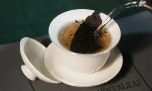Heißes Wasser fließt in eine Teetasse mit Pu-erh Tee. Mögliche Pu-erh Tee Nebenwirkungen sind selten, aber bei übermäßigem Genuss zu beachten.