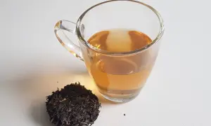 Ein Glas goldbrauner Pu-erh-Tee neben trockenen Teeblättern. Der Tee liefert sanftes Koffein für einen belebenden Start.