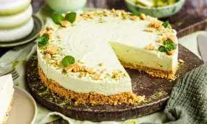 Ein cremiger Matcha Cheesecake mit Keksboden, garniert mit Minze und zerbröselten Keksen. Ein Stück wurde bereits angeschnitten.