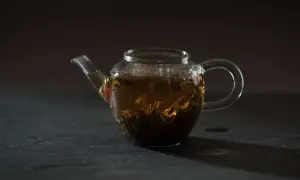 Glas-Teekanne mit braunem Tee und sichtbaren Tee-Inhaltsstoffen.