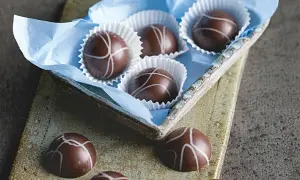 Schokoladenpralinen mit weißer Glasur, einige in einer blauen Papierschale, andere auf einer rustikalen Platte. Ein Genuss für Liebhaber von Matcha Pralinen.