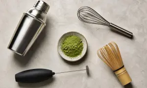 Matcha-Zubereitung: Pulver in Schale, daneben ein Milchaufschäumer, ein Schneebesen und ein Shaker. So gelingt Matcha ohne besen.