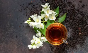 Ein Glas Jasmintee neben frischen Blüten und losem Tee. Jasmintee gesund und aromatisch.
