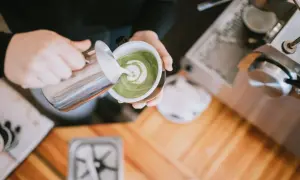 Barista verziert grünen Matcha-Tee mit Milchschaum. Perfekt für den Start in den Tag, auch auf leeren Magen.