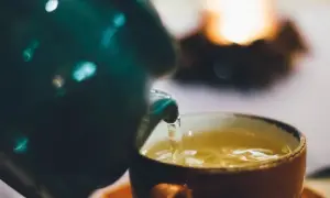 Ein grüner Teekrug gießt goldenen Tee in eine orangefarbene Tasse. Welcher Tee treibt nicht? Dieser hier, der Ruhe und Wärme verspricht.