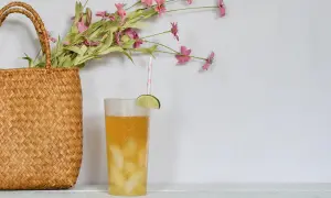 Erfrischender Drink mit Limette und Eis, daneben ein Korb mit Blumen. Perfekt, um Minztee selber zu machen und den Sommer zu genießen.