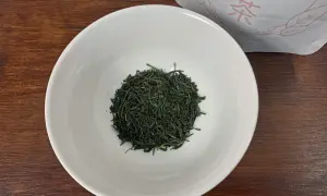 Trockene, dunkelgrüne Sencha-Teeblätter liegen in einer weißen Schale, bereit für die Zubereitung.