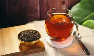 Eine Tasse heißer Ceylon Tee, reich an Koffein, neben einer Schale trockener Teeblätter.