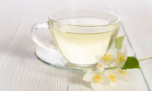 Eine Tasse klarer, heller Flüssigkeit, die an weißen Tee erinnert, mit duftenden Jasminblüten daneben.