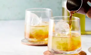 Zwei Gläser mit Eis und einem bernsteinfarbenen Getränk. Ein Jigger gießt Flüssigkeit in das vordere Glas. Ein erfrischender Gin mit Eistee.