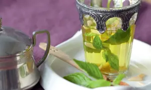 Ein Glas mit Minze ziehen lassen, daneben eine Teekanne.