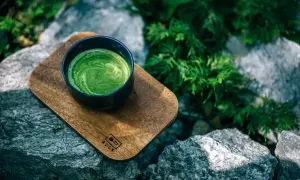 Eine Schale cremiger Matcha-Tee auf einem Holzbrett, umgeben von Steinen und Grün. Perfekt für eine ruhige Matcha-Stillzeit.