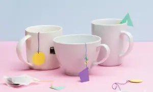 Drei Tassen mit selbstgemachten Teebeuteln, die mit bunten Anhängern verziert sind. Eine schöne Idee, um Teebeutel selber zu machen.
