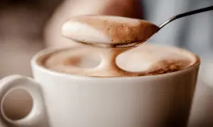 Ein Löffel voller Milchschaum über einer Tasse Kaffee. Der Koffein-Kick für den Magen.