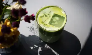 Ein Glas grüner Matcha mit Eiswürfel und einer Pflanze darauf. Neben dem Glas steht ein Strauß getrockneter Blumen. Mögliche matcha nebenwirkungen sind hier nicht ersichtlich.