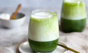 Zwei Gläser mit geschichtetem Matcha-Latte, die die perfekte Matcha-Zubereitung zeigen. Ein Löffel liegt daneben.