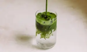 Ein leuchtend grüner Matcha-Sirup fließt in ein Glas mit Eis und sprudelndem Wasser. Ein erfrischender Matcha Tonic entsteht.
