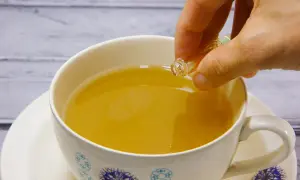 Eine Hand tropft eine Flüssigkeit aus einer kleinen Ampulle in eine Tasse Tee. Die ideale earl grey temperatur wird erreicht.