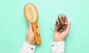 Hände halten Haarbürste und Haarbüschel. Ein Zeichen für Haarausfall, vielleicht nach dem Genuss von schwarzem Tee?