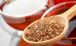 Rooibos Tee: Wirkung Schlafen. Eine Holzschaufel voller Rooibos-Blätter neben einer Tasse des roten Tees.