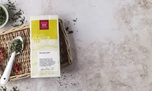 Kräutertee-Packung mit Löffel und Schale voller Kräuter. Die tee temperatur tabelle gibt Hinweise zur Zubereitung.