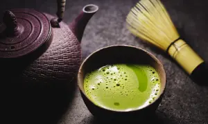 Eine traditionelle japanische Teekanne und ein Chasen (Bambusbesen) neben einer Schale mit schaumigem, leuchtend grünem Matcha. So wird Matcha zubereitet.