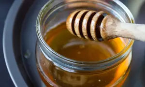 Ein Holzlöffel taucht in ein Glas mit flüssigem Honig. Perfekt zum Süßen von Tee.