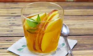 Ein Glas mit goldenem kamillentee mit honig, garniert mit Apfelscheiben und Minze, steht auf einem Holztisch.