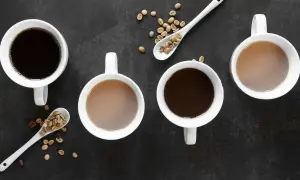 Vier Tassen Kaffee, zwei schwarz, zwei mit Milch, und Löffel mit Kaffeebohnen. Die Entscheidung zwischen Tee vs Kaffee ist hier klar: Kaffee!