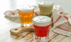 Drei Gläser mit bunten Getränken und cremiger Käseschaumhaube. Ein rotes, ein bernsteinfarbenes und ein grünes Cheese Tea.