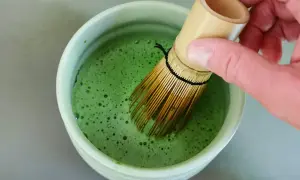 Hand whisking bright green matcha in a bowl. The ideal matcha temperatur is crucial for a smooth, frothy brew.
