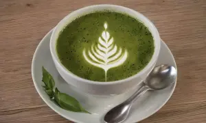 Ein cremiger Matcha Latte mit Latte Art, serviert auf einer Untertasse mit Löffel und grünen Blättern. Perfekt für ein Matcha Kaffee Rezept.
