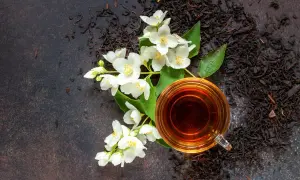 Eine Tasse Jasmintee neben frischen Blüten. Die beruhigende Jasmin tee wirkung macht ihn zum perfekten Genuss.