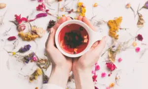 Hände halten eine Tasse mit rotem Tee, umgeben von getrockneten Blumen. Ein perfekter Tee am Morgen für einen frischen Start.