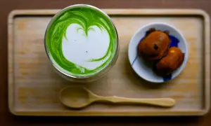 Ein Glas cremiger Matcha mit Herz-Latté-Art und zwei süßen Leckereien. Perfekt zum Matcha trinken.
