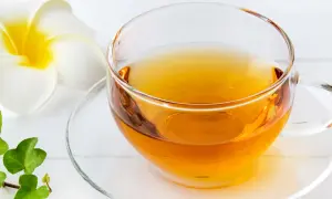 Klarer schwarzer Tee in einer Glas Tasse, beruhigend für den Magen, neben einer weißen Blüte und grünen Blättern.
