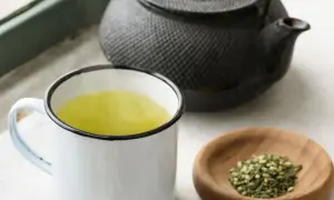 Dampfender Genmaicha in einer Tasse, daneben eine Teekanne und eine Schale mit geröstetem Reis. Die Genmaicha Zubereitung ist im Gange.
