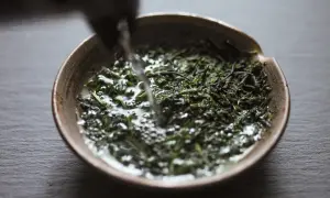 Wasser fließt in eine Schale mit grünen Teeblättern für die Gyokuro Zubereitung.