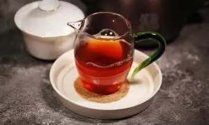 Ein Glas mit Oolong Tee, dessen Farbe an einen Krebs erinnert, steht auf einem Untersetzer. Daneben eine weiße Teedose.