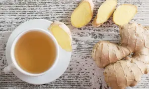 Eine Tasse Ingwertee und frische Ingwerstücke auf holzigem Hintergrund. Perfekt für einen beruhigenden Ingwer abends.