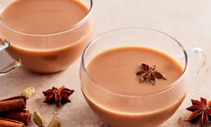 Zwei Tassen cremiger Chai Latte, garniert mit Sternanis. Zimtstangen und Kardamomkapseln deuten auf ein authentisches indischer chai rezept hin.