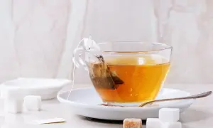 Eine Tasse Tee mit einem Teebeutel, der aussieht, als wäre der abgelaufene Tee schon lange im Wasser. Zuckerwürfel liegen daneben.