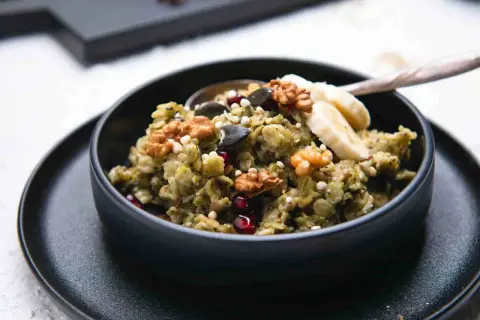 Grüner, cremiger matcha porridge mit Nüssen, Kernen, Granatapfel und Bananenscheiben. Ein gesundes Frühstück.