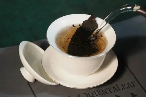 Heißes Wasser fließt in eine Teetasse mit Pu-erh Tee. Mögliche Pu-erh Tee Nebenwirkungen sind selten, aber bei übermäßigem Genuss zu beachten.