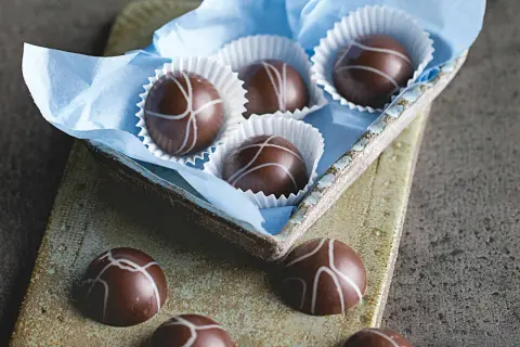 Schokoladenpralinen mit weißer Glasur, einige in einer blauen Papierschale, andere auf einer rustikalen Platte. Ein Genuss für Liebhaber von Matcha Pralinen.