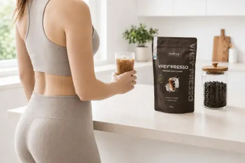 Frau hält Eiskaffee, neben VHEY® PRESSO Protein-Pulver. Die Koffein-Wirkdauer wird durch den belebenden Drink unterstützt.
