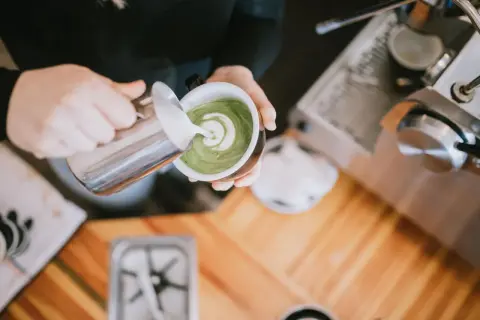Barista verziert grünen Matcha-Tee mit Milchschaum. Perfekt für den Start in den Tag, auch auf leeren Magen.