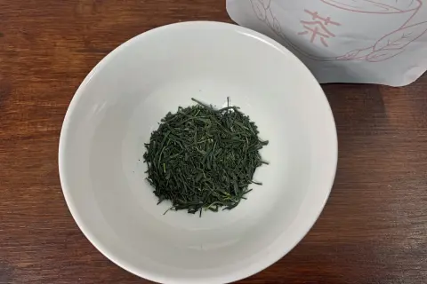Trockene, dunkelgrüne Sencha-Teeblätter liegen in einer weißen Schale, bereit für die Zubereitung.
