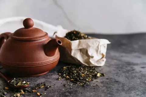 Braune Teekanne mit losem Tee und einem Löffel, bereit für den Aufguss Tee.