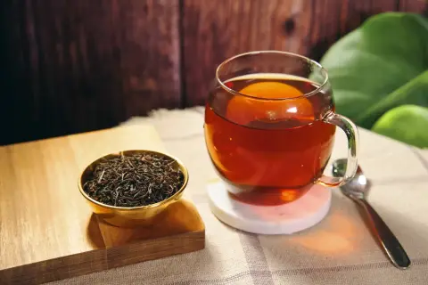 Eine Tasse heißer Ceylon Tee, reich an Koffein, neben einer Schale trockener Teeblätter.